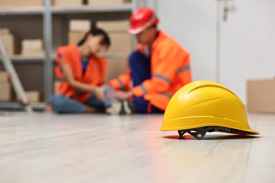 Photo of Accident at work. Hardhat on floor and man helping his injured colleague in warehouse, selective focus