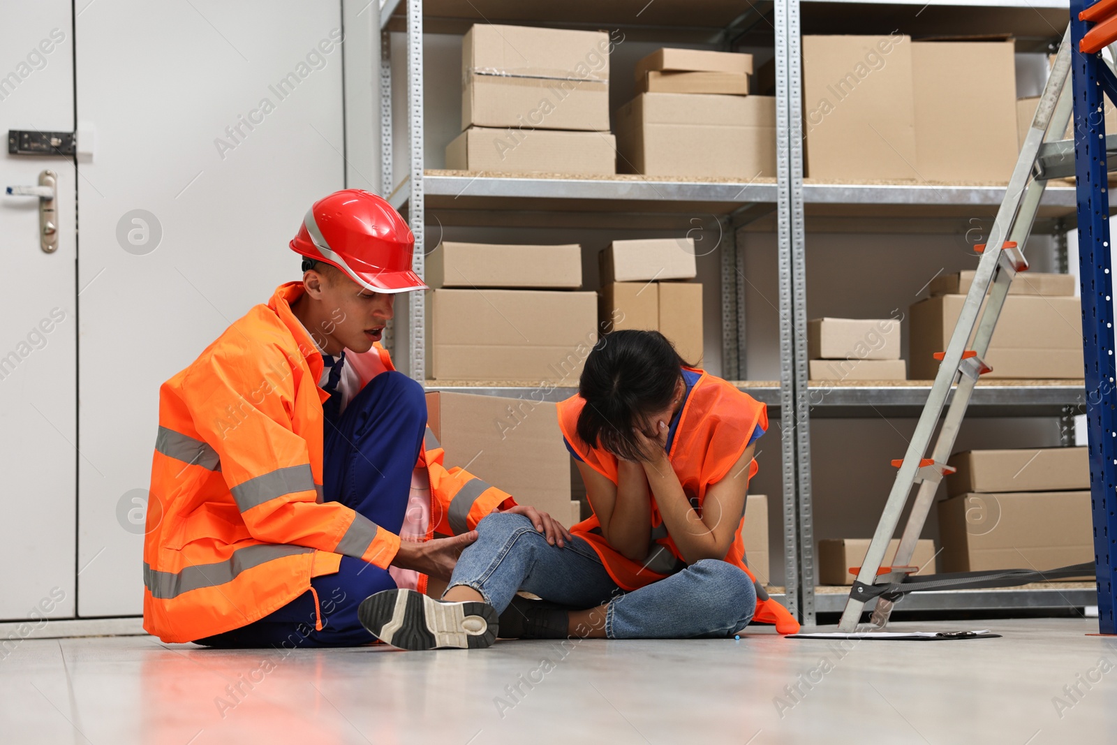 Photo of Accident at work. Man helping his injured colleague in warehouse