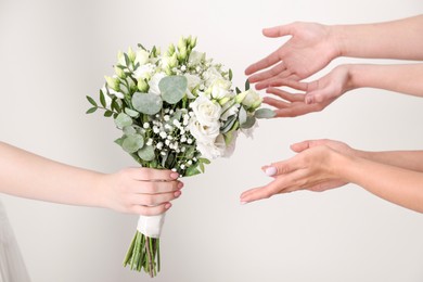 Photo of Bridesmaids giving beautiful wedding bouquet to bride on light background, closeup