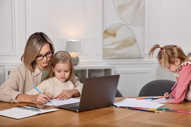 Photo of Work-family balance. Single mother with her children drawing at wooden table indoors