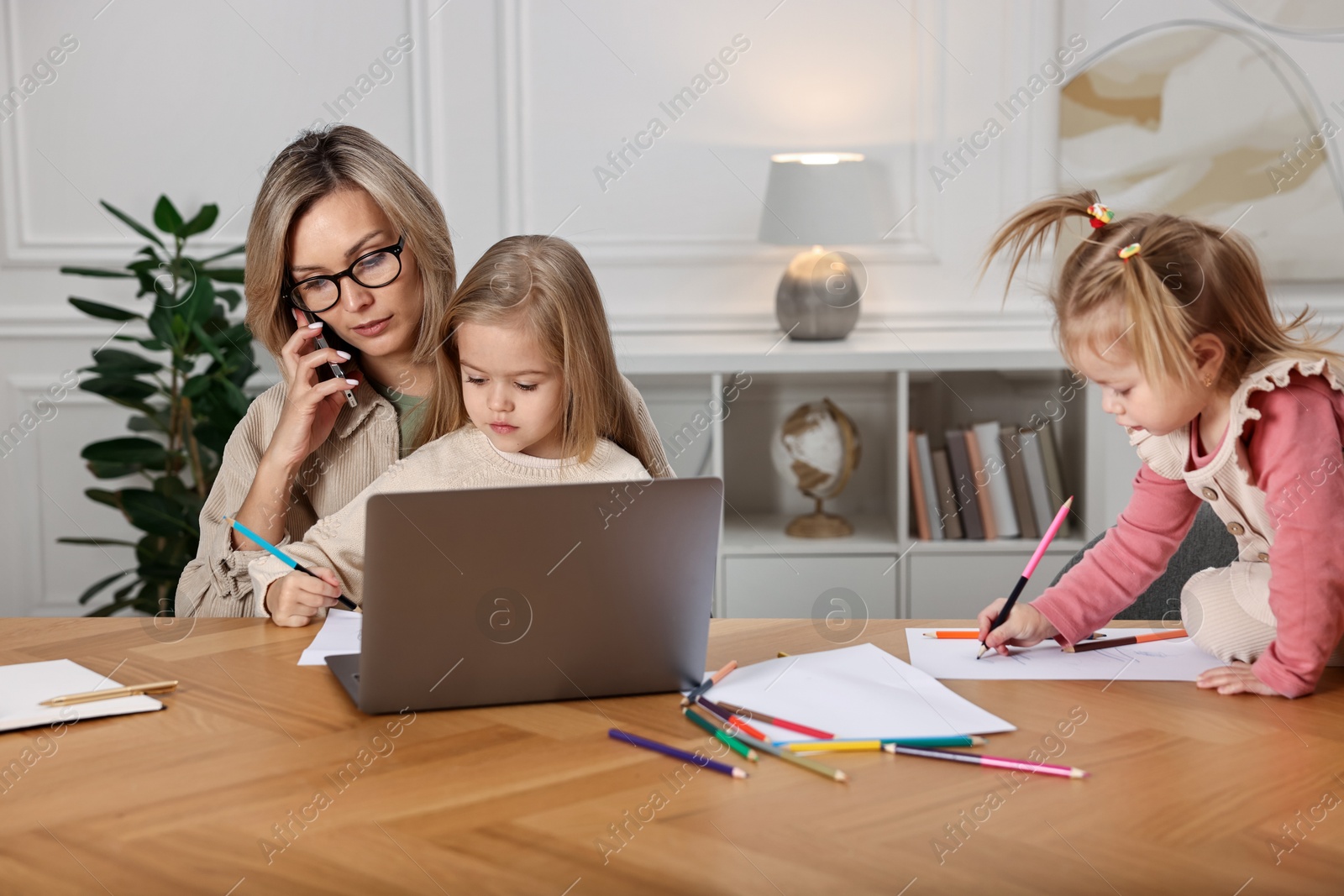 Photo of Work-family balance. Single mother talking by smartphone and her children drawing at wooden table indoors