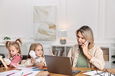 Photo of Work-family balance. Single mother talking by smartphone and refusing to play with her children at wooden table indoors