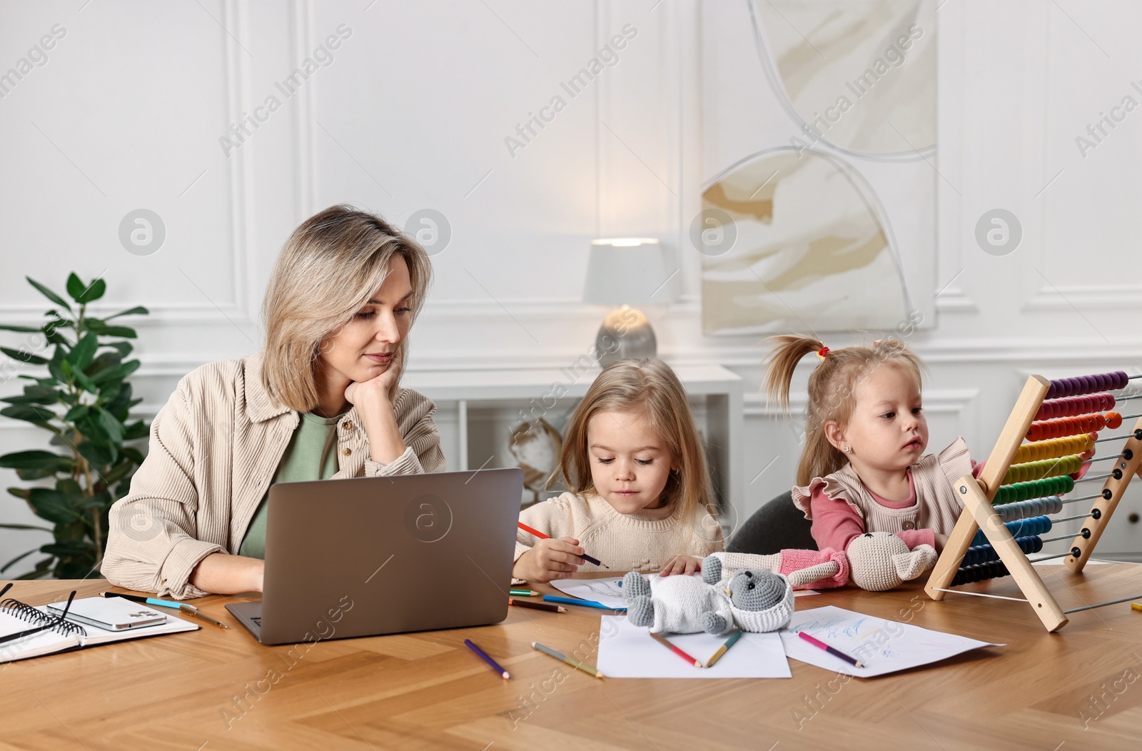 Photo of Single mother working and her children drawing at wooden table indoors