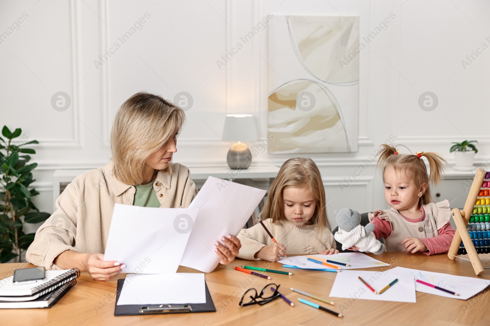 Photo of Single mother working and her children drawing at wooden table indoors