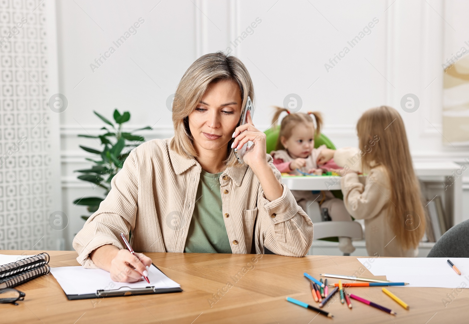 Photo of Work at home. Single mother talking by smartphone while her children playing indoors, selective focus