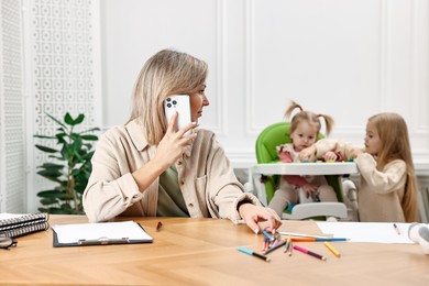 Photo of Work at home. Single mother talking by smartphone while her children playing indoors, selective focus