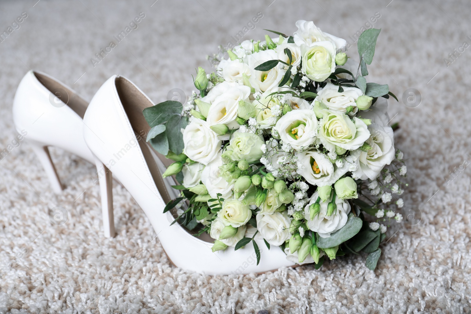 Photo of Wedding bouquet of beautiful flowers and bridal shoes on beige carpet, closeup