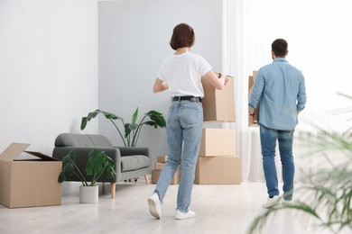 Photo of Moving day. Couple with cardboard boxes in their new home, back view