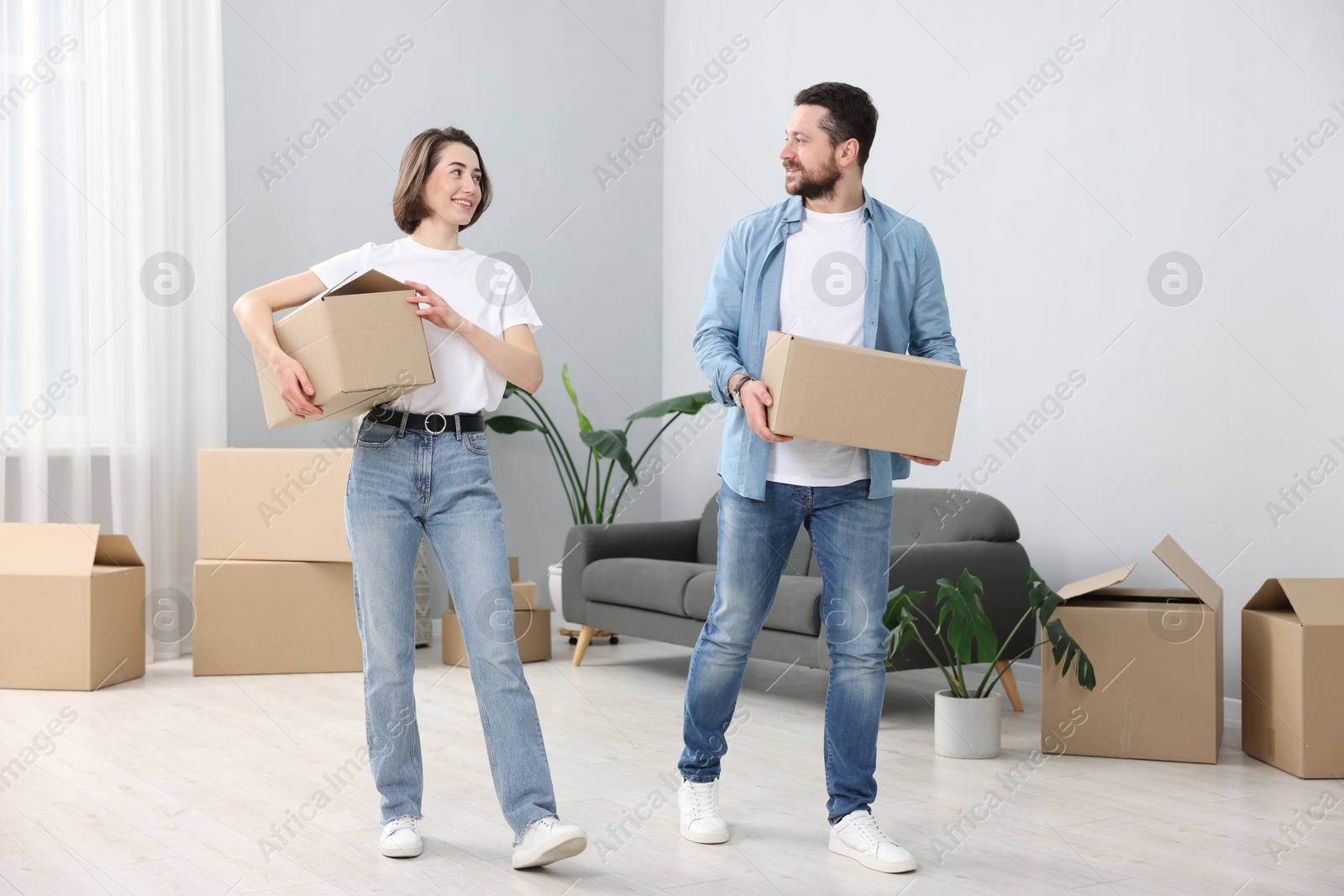 Photo of Moving day. Happy couple with cardboard boxes in their new home