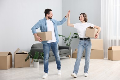 Photo of Moving day. Happy couple with cardboard boxes giving each other high five in their new home