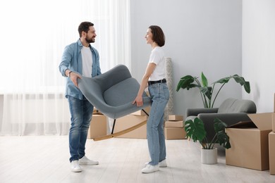 Moving day. Happy couple carrying chair in their new home