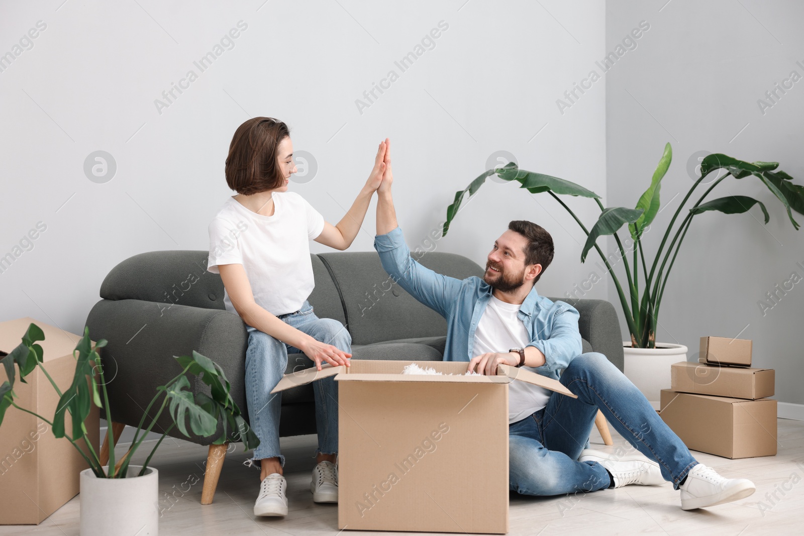 Photo of Moving day. Happy couple with cardboard box giving each other high five in their new home