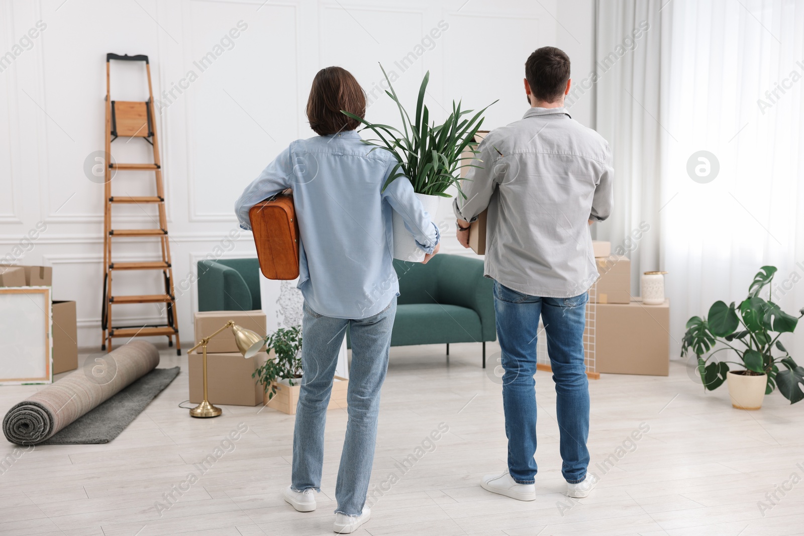 Photo of Moving day. Couple with their belongings in new home, back view