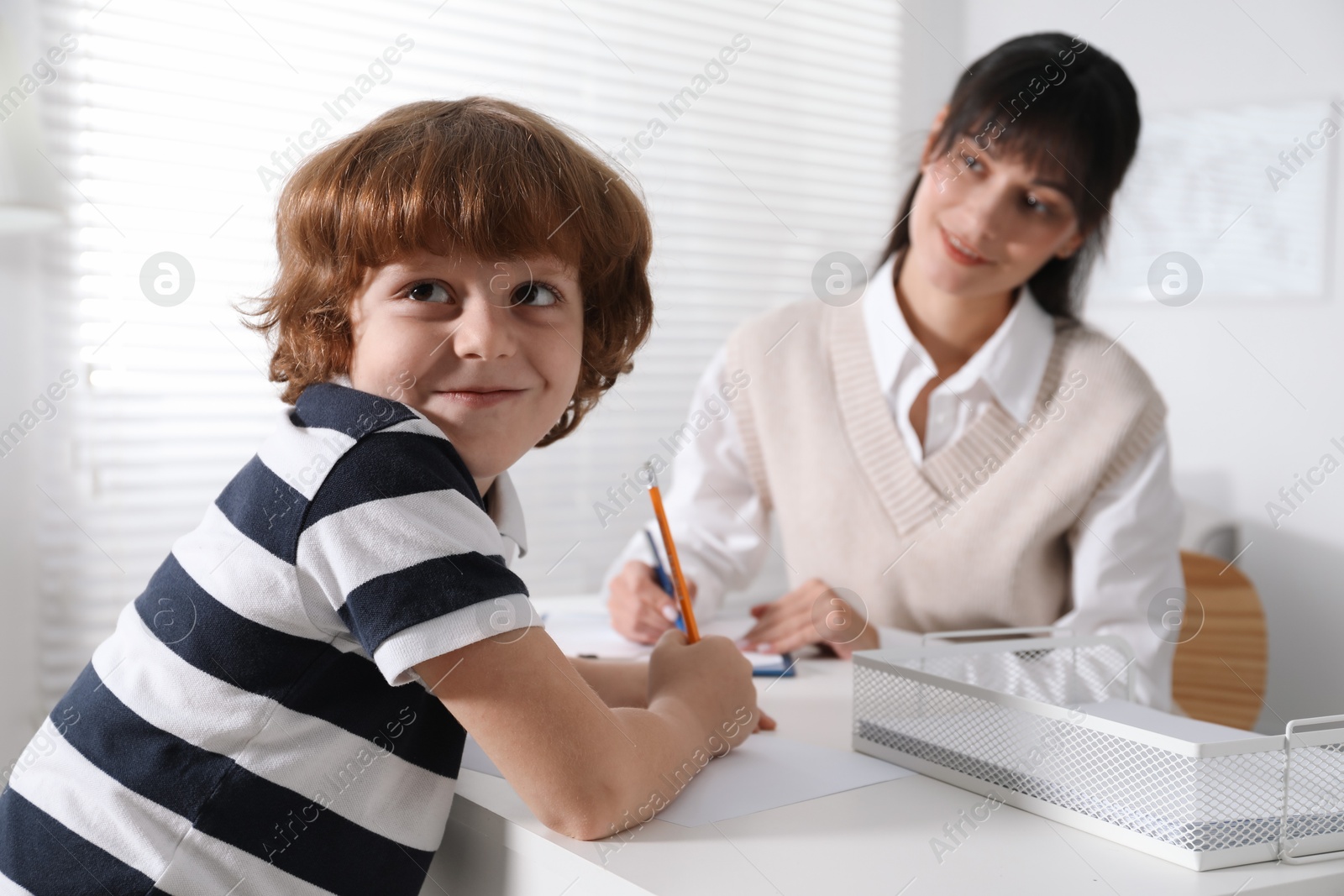 Photo of Little boy writing something at desk while psychologist taking notes, selective focus