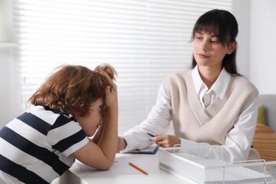 Photo of Psychologist comforting little boy at desk in office, selective focus