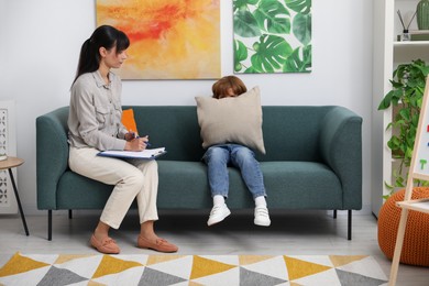 Photo of Upset little boy having therapy session with psychologist in office