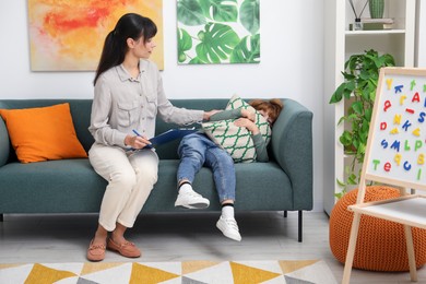 Photo of Upset little boy having therapy session with psychologist in office