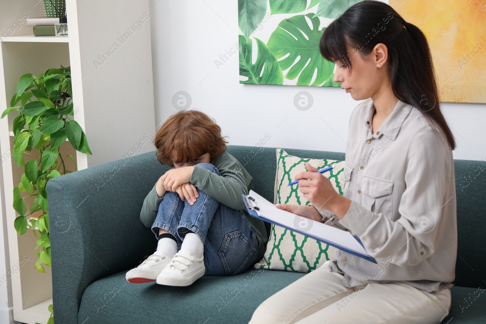 Photo of Upset little boy having therapy session with psychologist in office