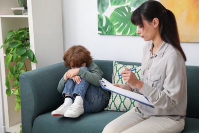 Photo of Upset little boy having therapy session with psychologist in office