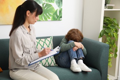 Photo of Upset little boy having therapy session with psychologist in office