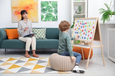 Photo of Boy assembling letters on magnetic board while psychologist taking notes indoors