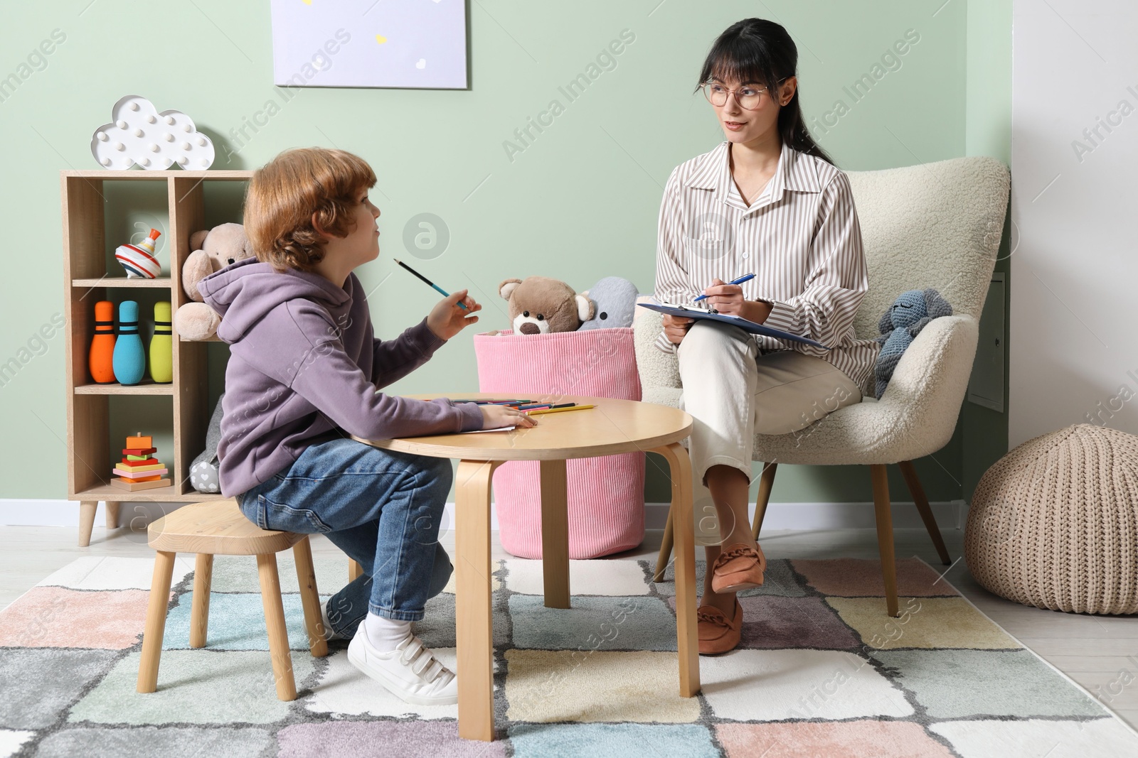 Photo of Boy drawing at table during consultation with psychologist indoors