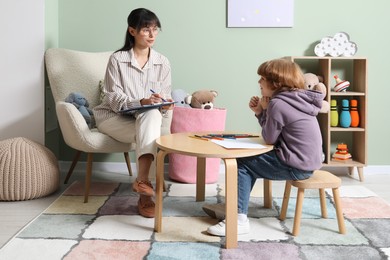 Photo of Boy drawing at table during consultation with psychologist indoors