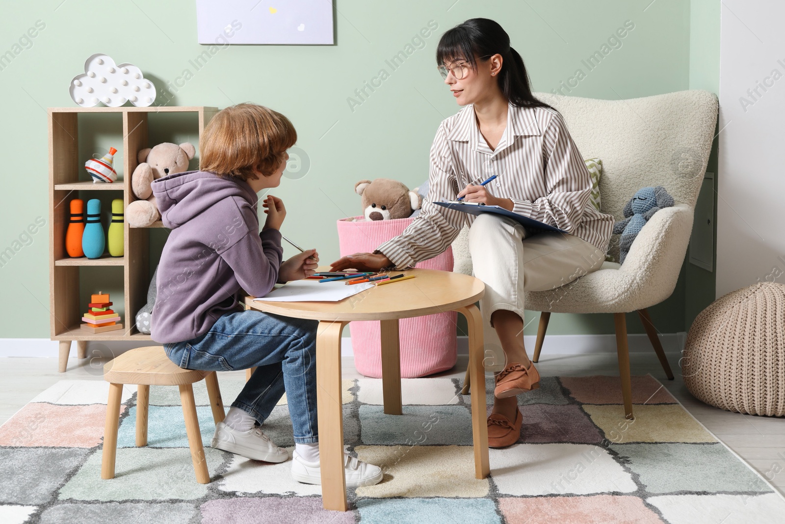 Photo of Boy drawing at table during consultation with psychologist indoors