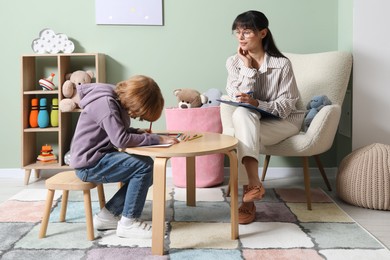 Photo of Boy drawing at table during consultation with psychologist indoors