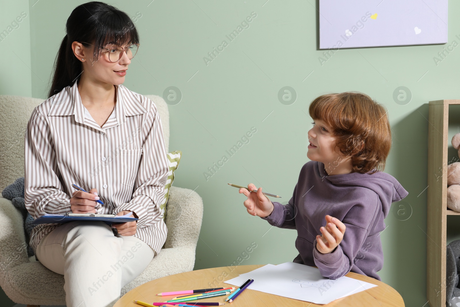 Photo of Boy drawing at table during consultation with psychologist indoors