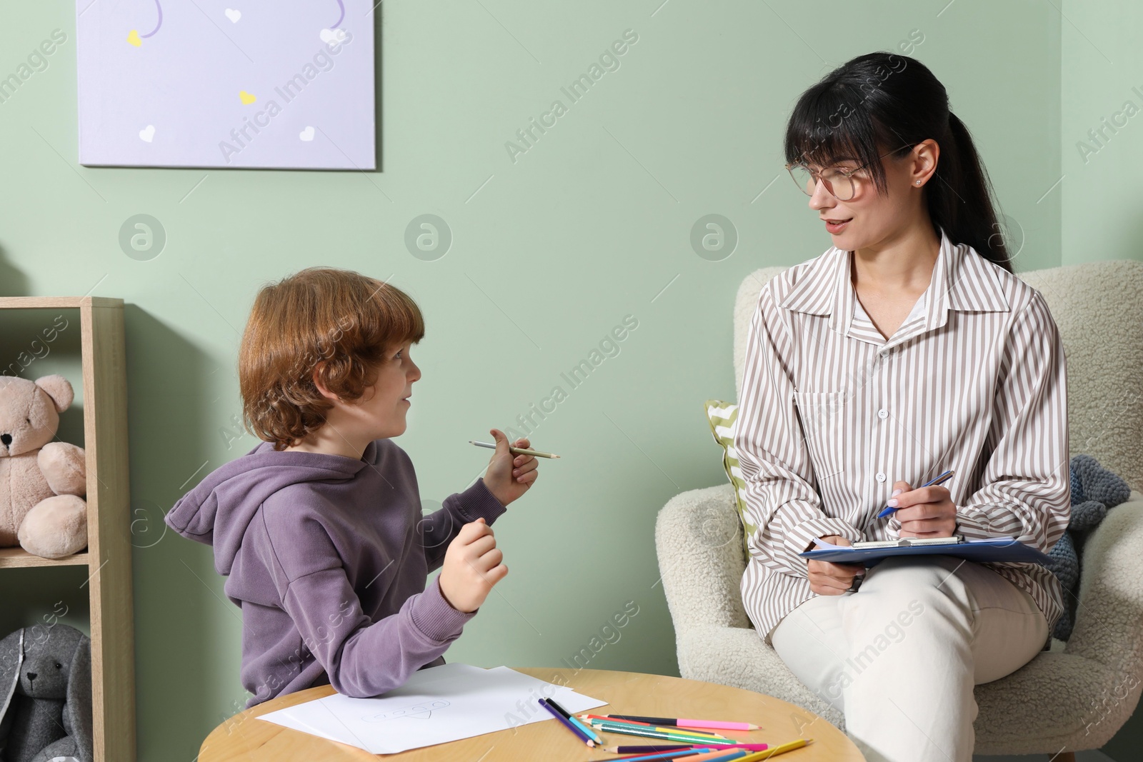 Photo of Boy drawing at table during consultation with psychologist indoors