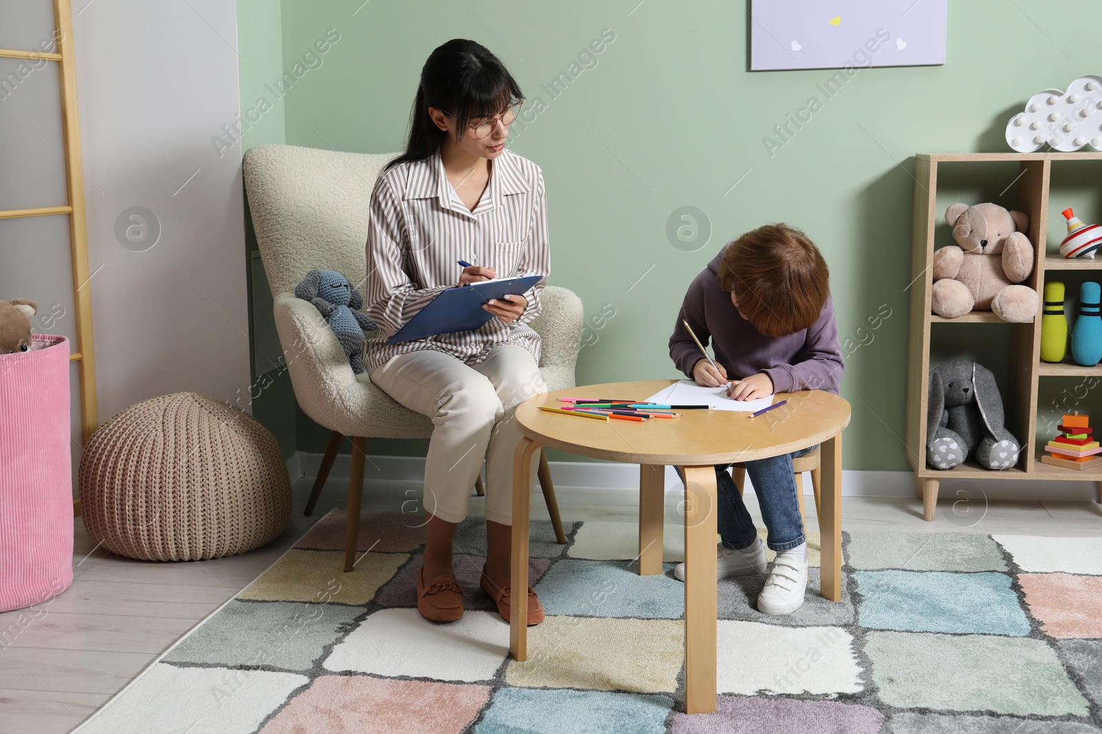 Photo of Boy drawing at table during consultation with psychologist indoors