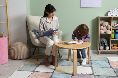 Photo of Boy drawing at table during consultation with psychologist indoors