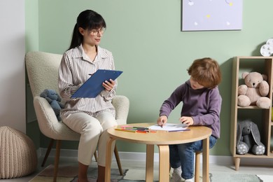 Photo of Boy drawing at table during consultation with psychologist indoors