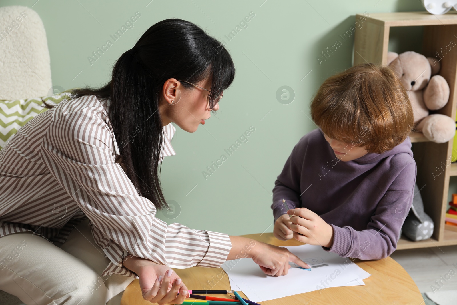 Photo of Boy drawing at table during consultation with psychologist indoors