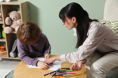 Photo of Boy drawing at table during consultation with psychologist indoors