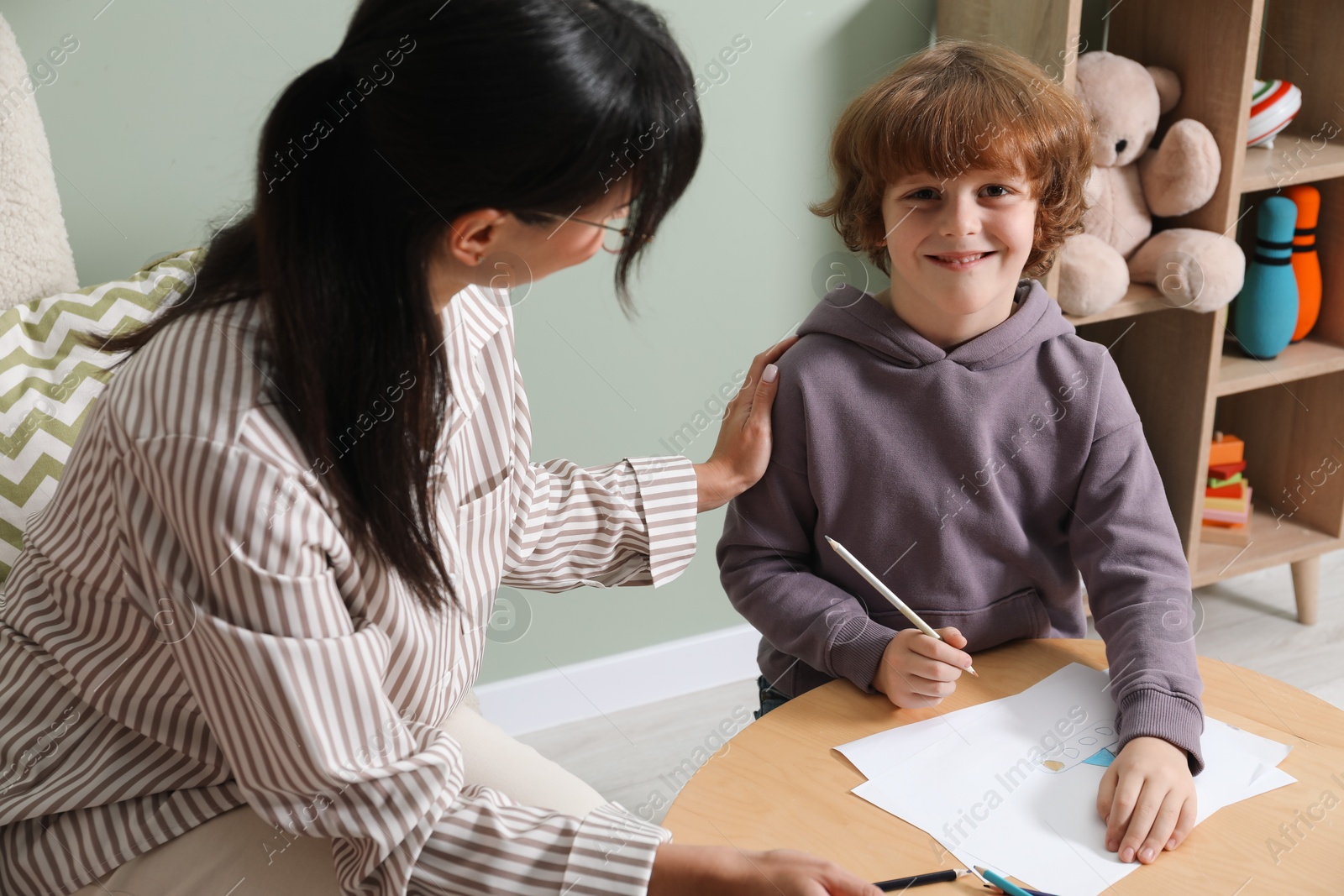 Photo of Boy drawing at table during consultation with psychologist indoors