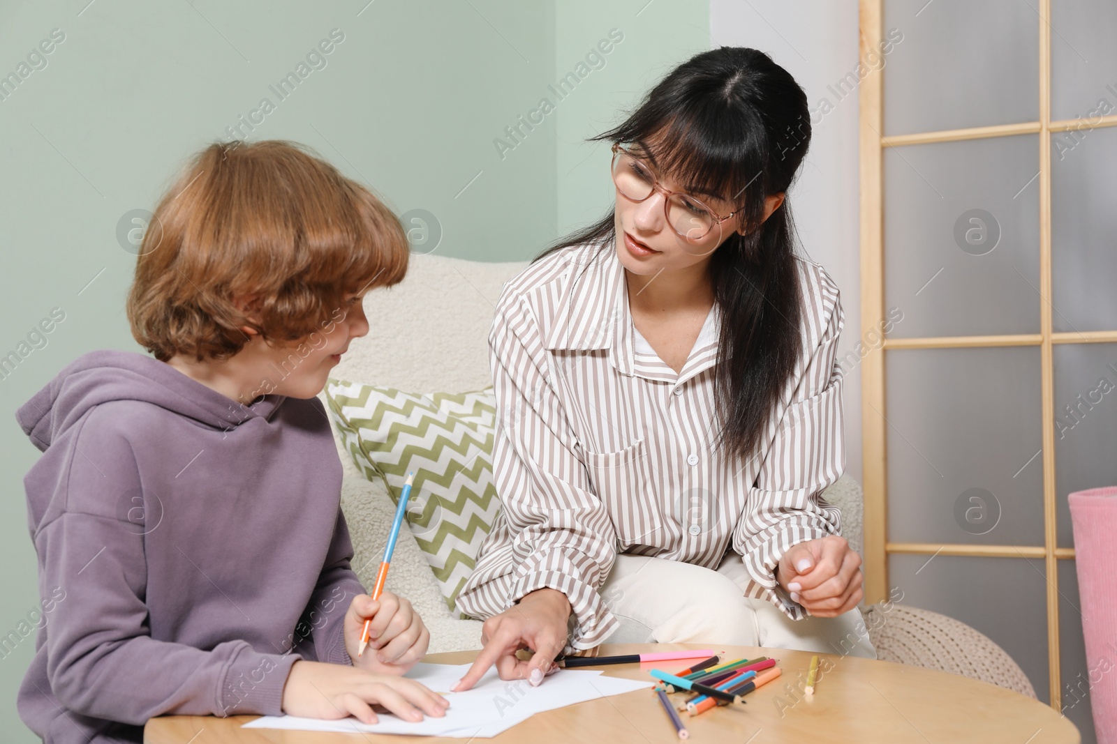 Photo of Boy drawing at table during consultation with psychologist indoors