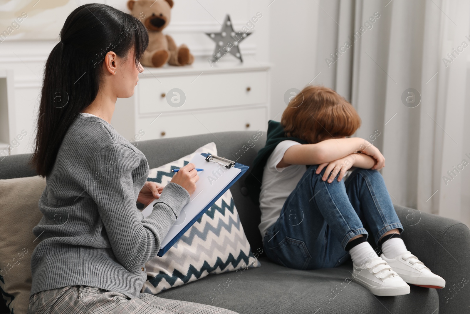 Photo of Upset little boy having therapy session with psychologist in office