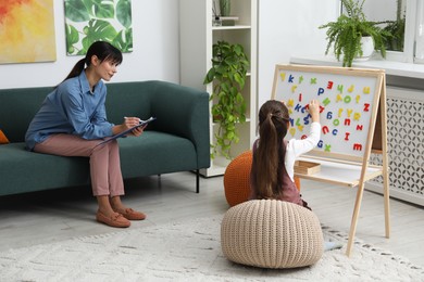 Photo of Girl assembling letters on magnetic board while psychologist taking notes indoors