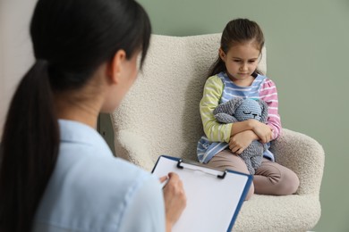 Photo of Psychologist having therapy session with little girl in office, selective focus