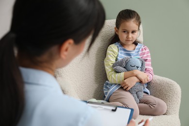 Photo of Psychologist having therapy session with little girl in office, selective focus