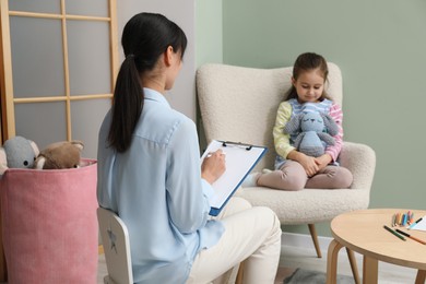 Photo of Psychologist having therapy session with little girl in office, selective focus