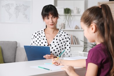 Photo of Little girl drawing at desk while psychologist taking notes, selective focus