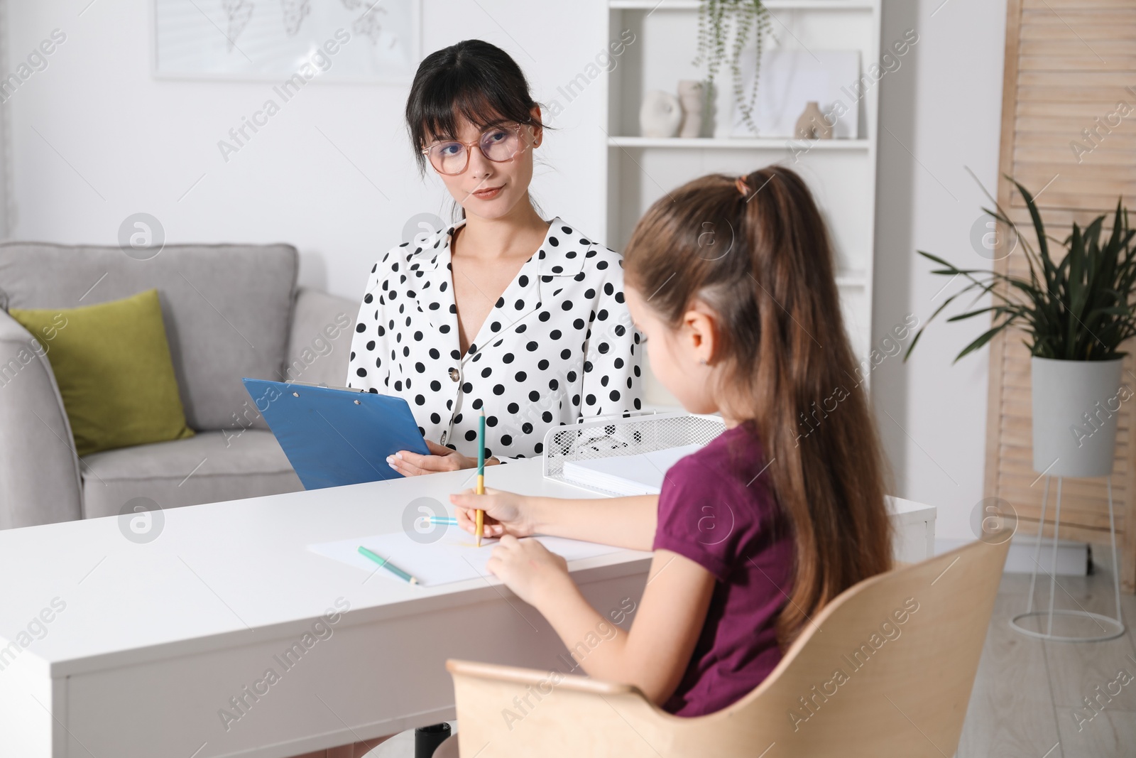 Photo of Little girl drawing at desk while psychologist taking notes, selective focus