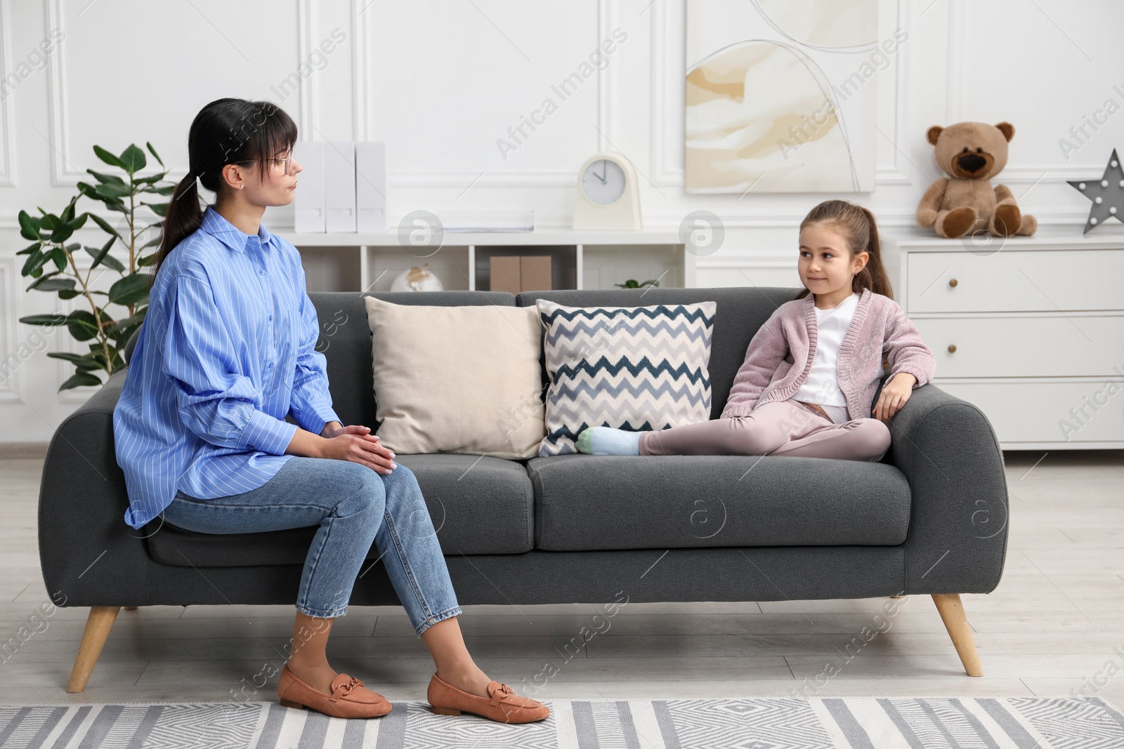 Photo of Psychologist having therapy session with little girl on sofa in office