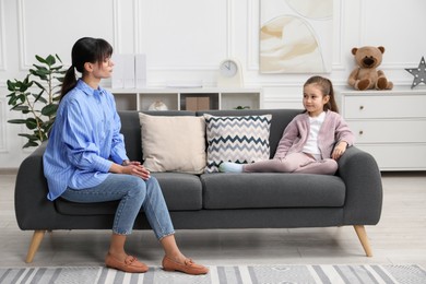 Photo of Psychologist having therapy session with little girl on sofa in office