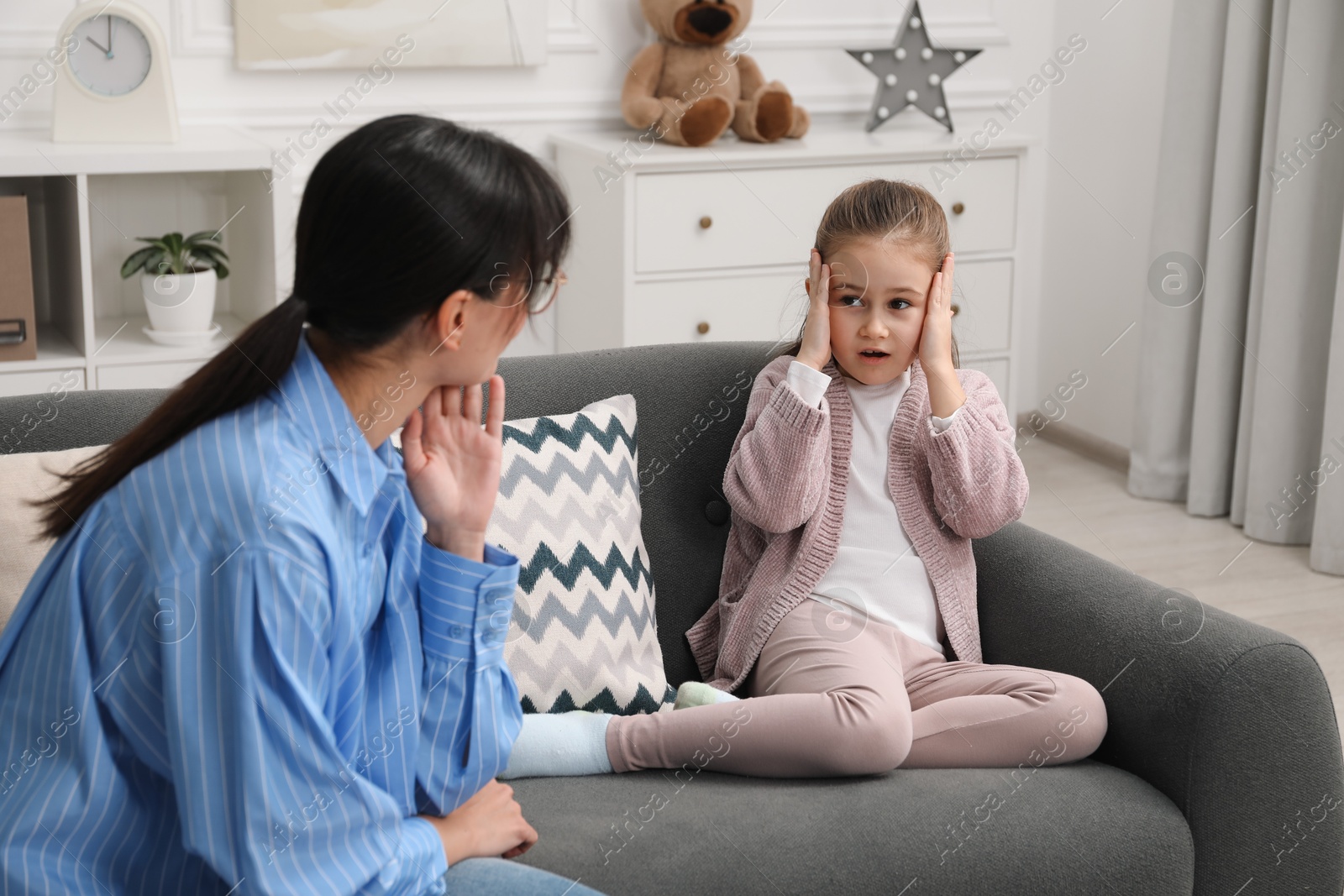 Photo of Psychologist having therapy session with little girl on sofa in office