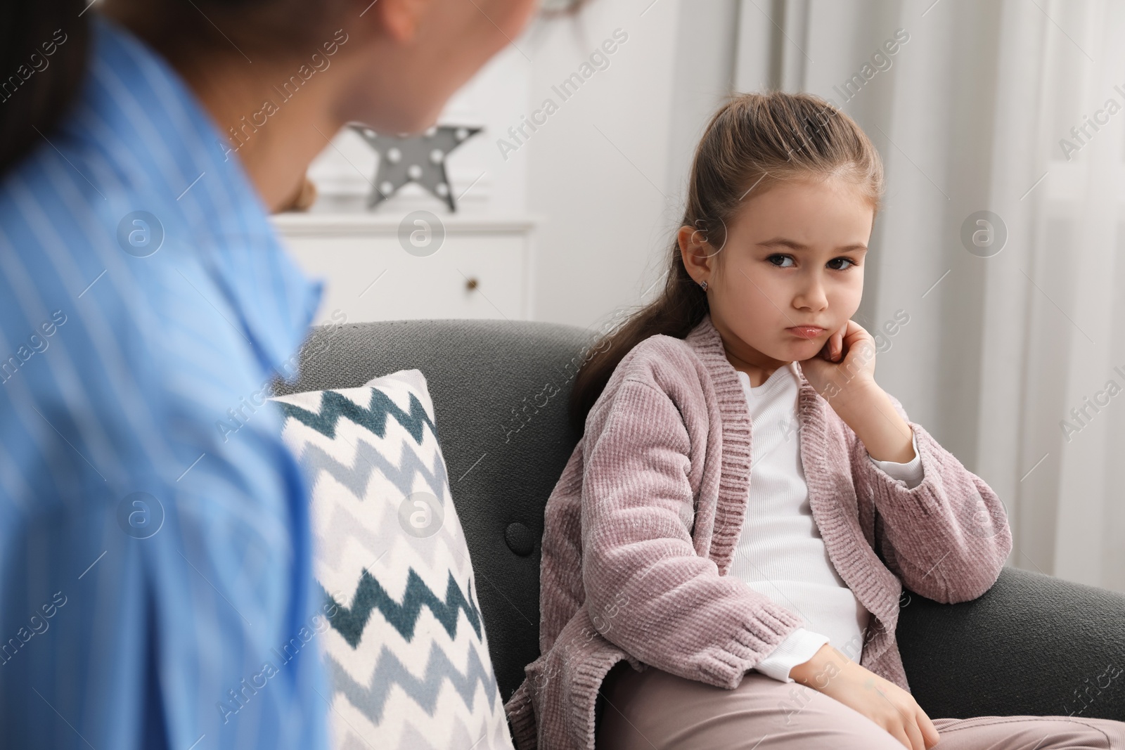 Photo of Psychologist having therapy session with little girl on sofa in office