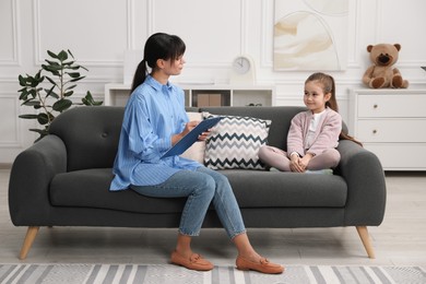 Photo of Psychologist having therapy session with little girl on sofa in office